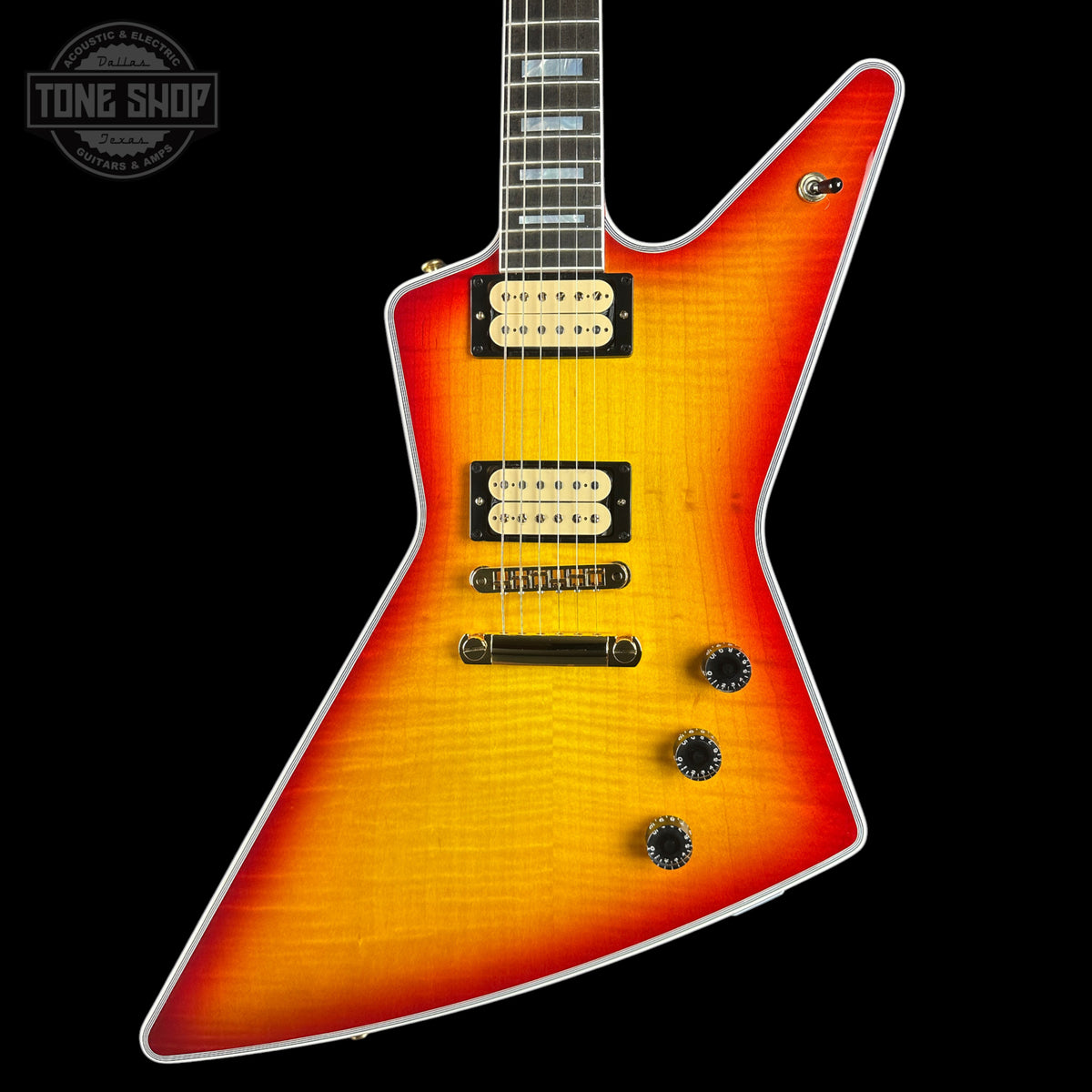 A classic electric guitar with a distinctive angular body, featuring a vibrant sunburst finish that transitions from bright orange in the center to a deep red edge, set against a solid black background.