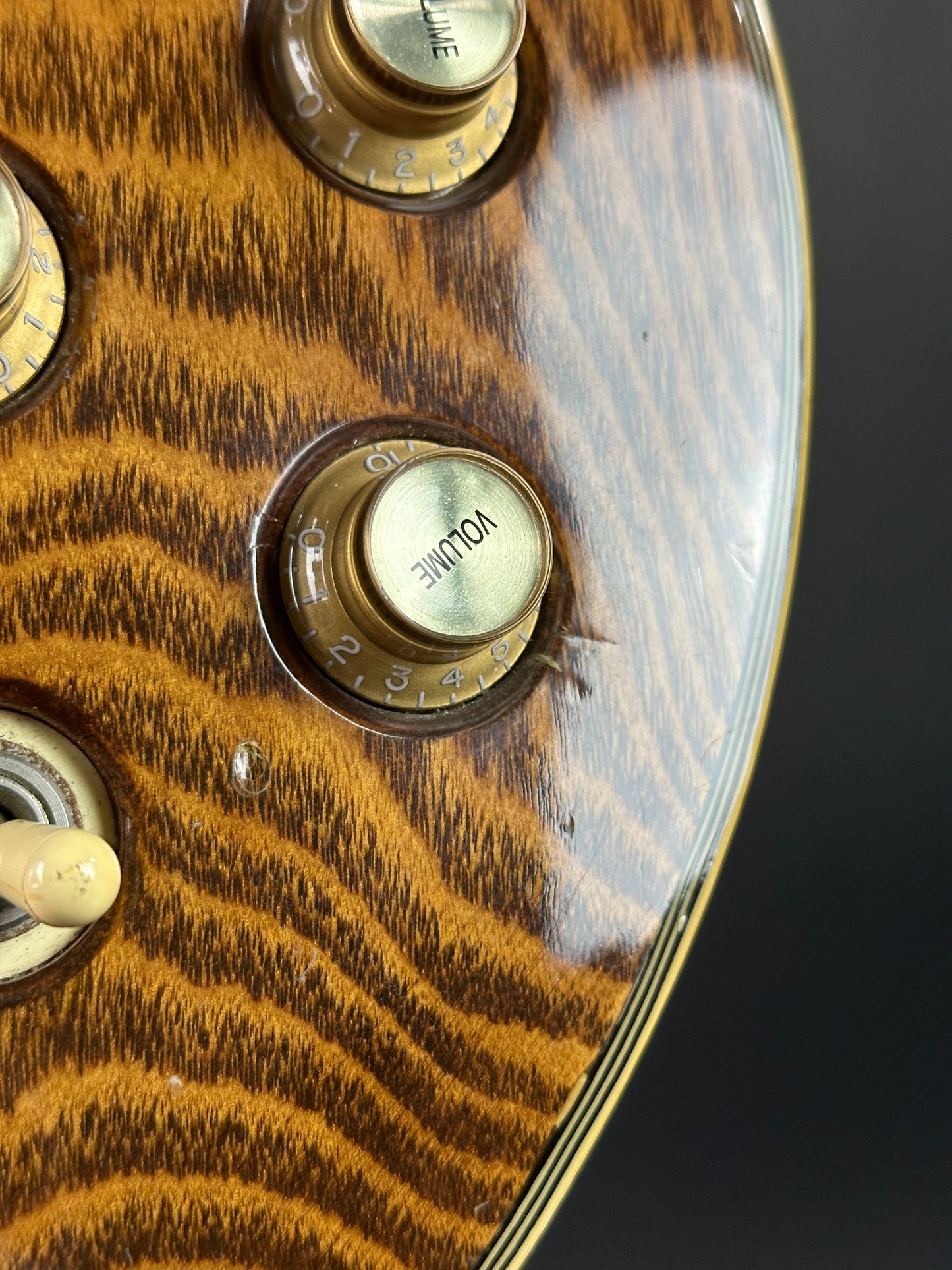 Close-up of a guitar control panel with volume knobs on a wooden surface.