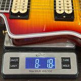 A close-up of a guitar body resting on a digital scale to show weight. The scale displays 8 lb 18 oz.