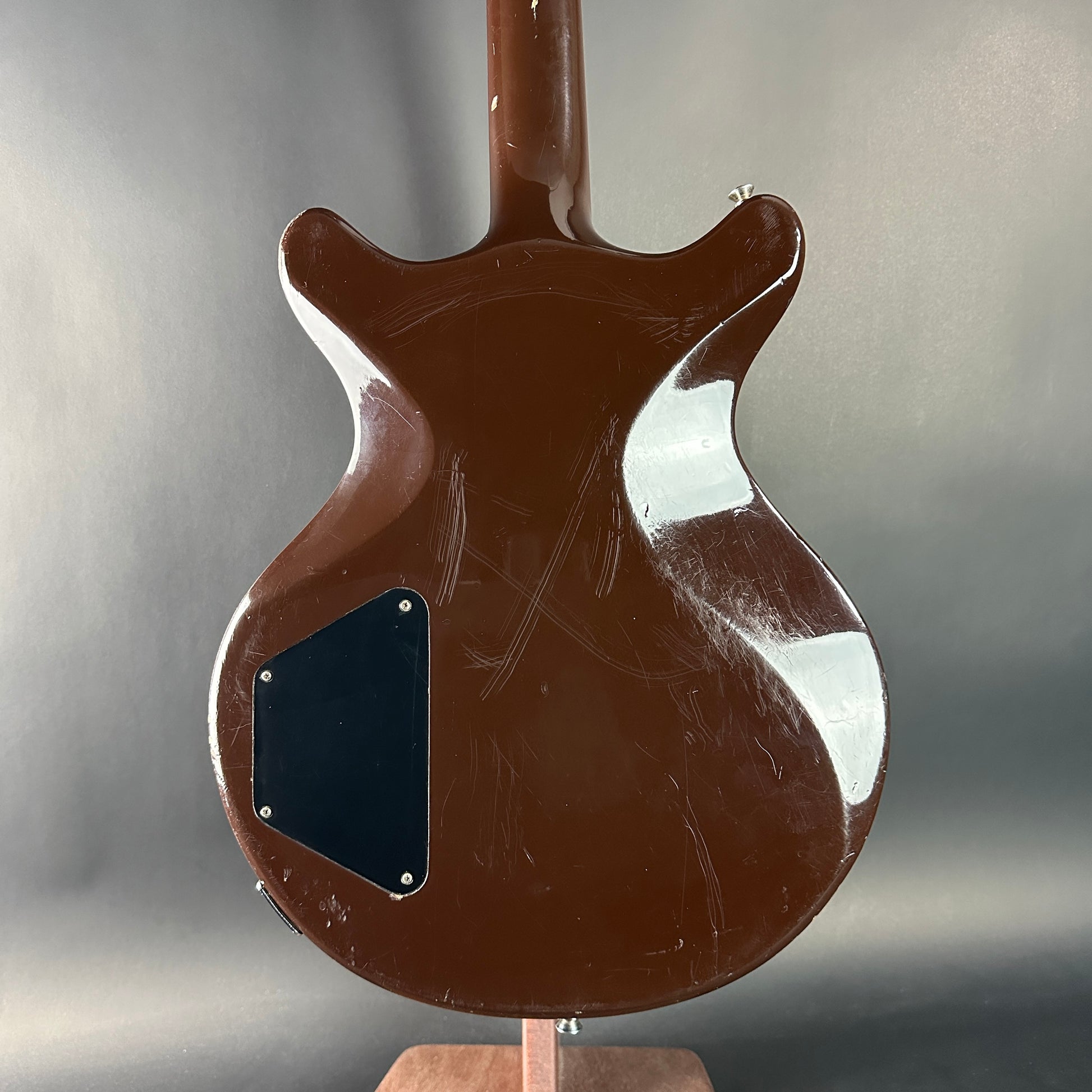 Brown electric guitar on a stand with a gray background