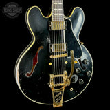 A black Gibson electric guitar with gold hardware and trim, shown against a solid black background. The body has visible wear and scuffs, and a 'Tone Shop' watermark is visible in the top left corner.