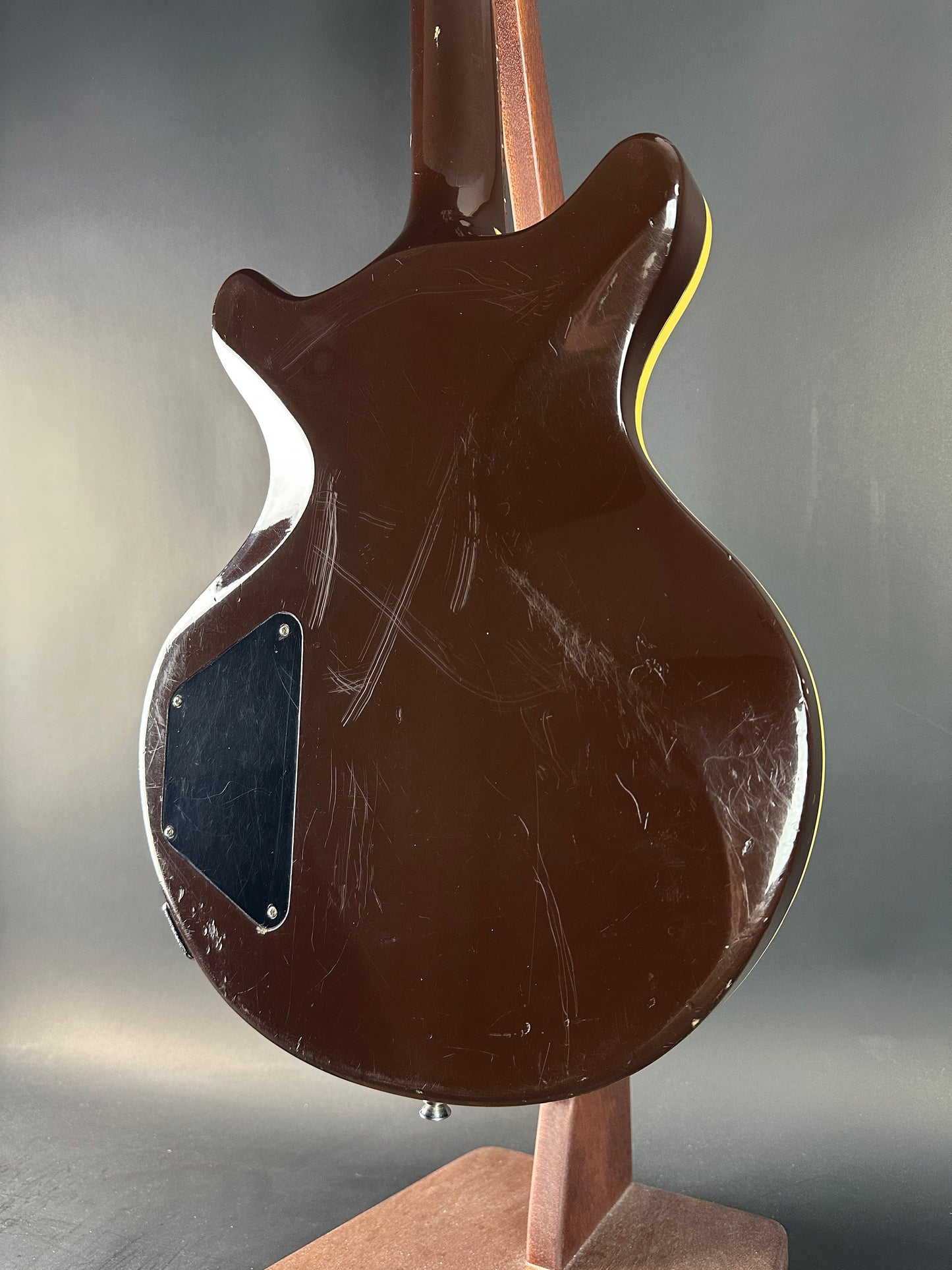 Close-up of a brown electric guitar with visible wear on a gray background