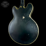 The back of a black electric guitar with a gold outline border, showing significant wear, scratches, and scuffs on the glossy finish, set against a solid black background.