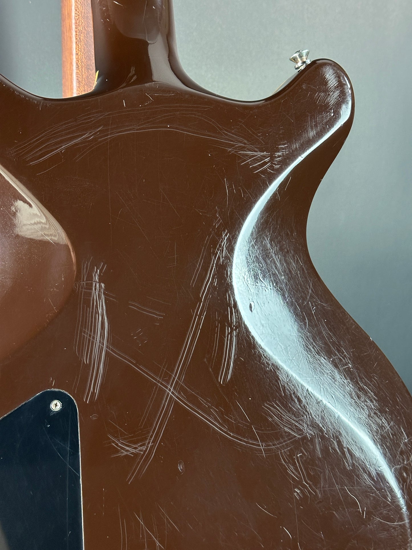 Close-up of a guitar's back with visible wear and tear on a gray background