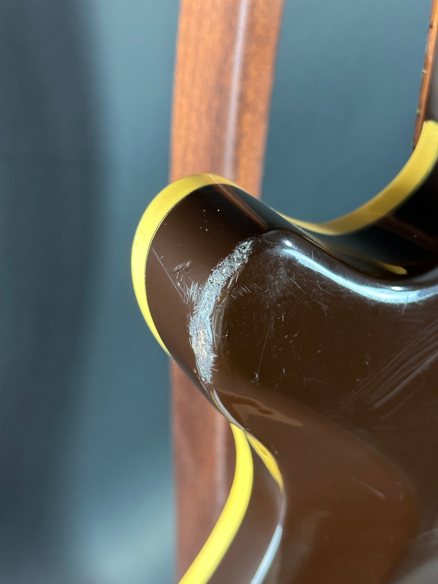 Close-up of a guitar's neck and headstock with a dark finish and yellow binding.