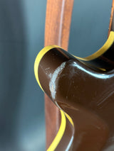Close-up of a guitar's neck and headstock with a dark finish and yellow binding.