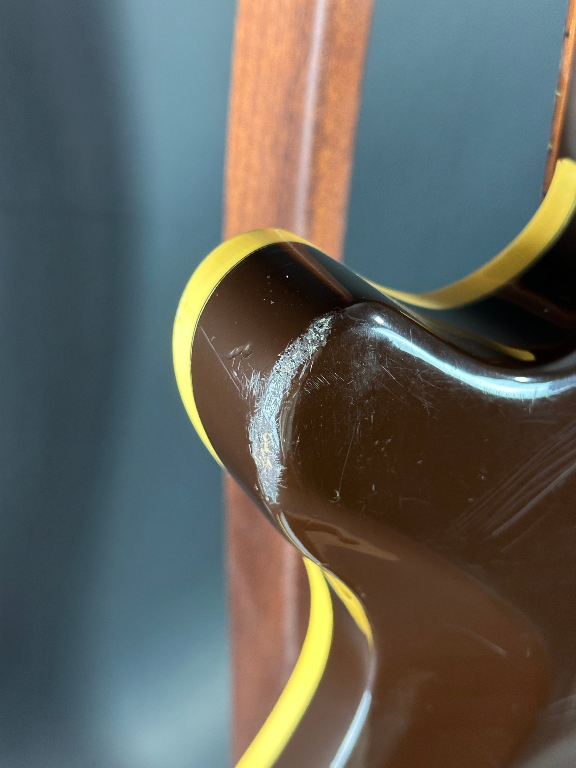 Close-up of a guitar's neck and headstock with a dark finish and yellow binding.