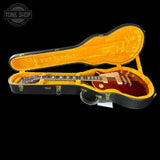 A red Gibson Les Paul Custom electric guitar displayed inside an open black hard case with a bright yellow-orange velvet interior, set against a solid black background.