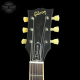 Close-up of a Gibson Les Paul Deluxe acoustic guitar headstock against a black background, showing the Gibson logo, Les Paul Model text, and six tuning pegs.
