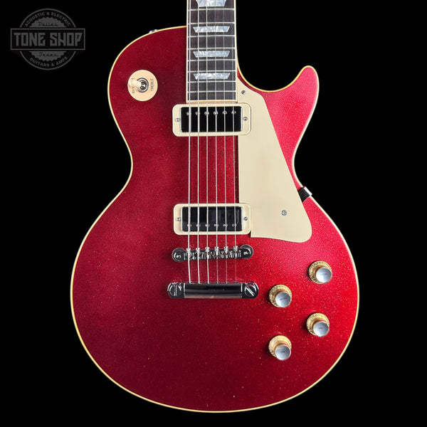 A red glitter electric guitar with a cream pickguard and gold-toned hardware, shown against a solid black background. A 'TONE SHOP' watermark is visible in the top-left corner.