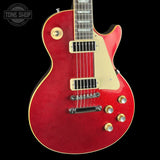 A red electric guitar with gold hardware and a cream pickguard, shown against a solid black background. A Tone Shop watermark is visible in the top-left corner.