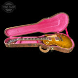 A gold-top electric guitar resting inside an open hard case with a bright pink velvet interior, shown against a black background. A Tone Shop watermark is visible in the upper left corner.