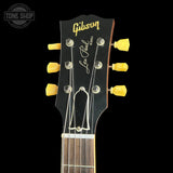 Close-up of a Gibson Les Paul Standard electric guitar headstock, showing the gold Gibson logo, 'Les Paul Standard' script, six yellow tuning pegs, and the neck beginning against a black background.