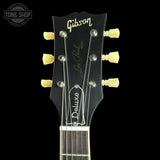 Close-up of the headstock of a Gibson Les Paul Deluxe electric guitar against a black background, showing the Gibson logo, Les Paul signature, and Deluxe model name.