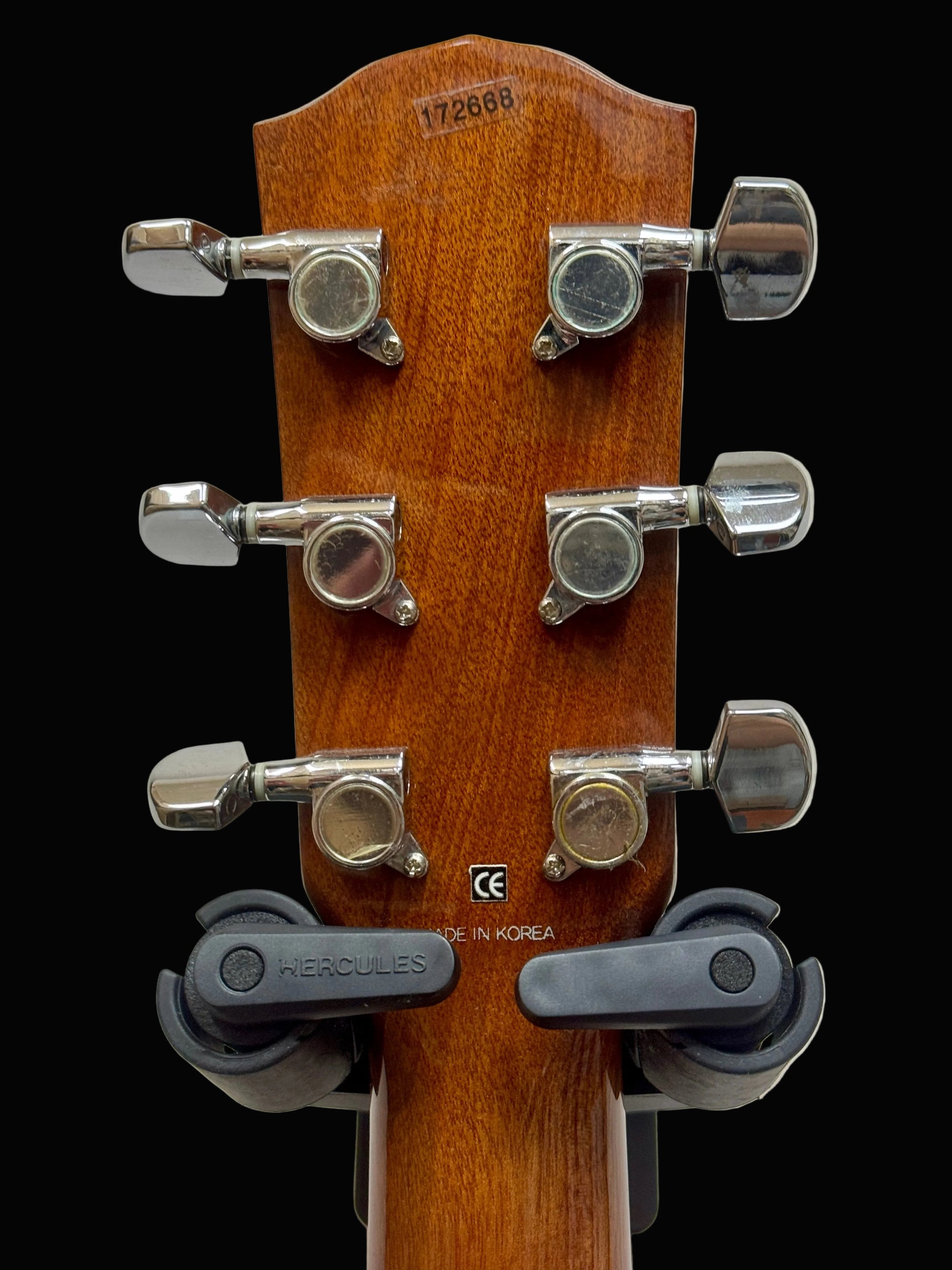 Guitar headstock with tuning pegs and brand name on a light gray background