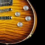 Close-up of an electric guitar body showing a sunburst finish with a prominent flamed maple wood grain, chrome hardware, and clear textured knobs against a black background.