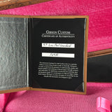 An open Gibson Custom Certificate of Authenticity booklet for a 57 Les Paul Standard, showing the black certificate insert with handwritten serial number 76930, placed on a pink velvet surface.