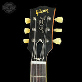 Close-up of a Gibson Les Paul Standard acoustic guitar headstock in black, featuring gold Gibson branding, a white script Les Paul signature, and cream-colored tuning pegs against a black background.