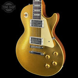 A gold glitter electric guitar with a cream pickguard, chrome hardware, and a brown wood body edge, shown against a black background with a Tone Shop watermark in the top-left corner.