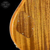 Close-up of the back of an electric guitar showing a glossy warm brown wood finish and a cutout for the pickup, with a Tone Shop watermark in the top left corner.