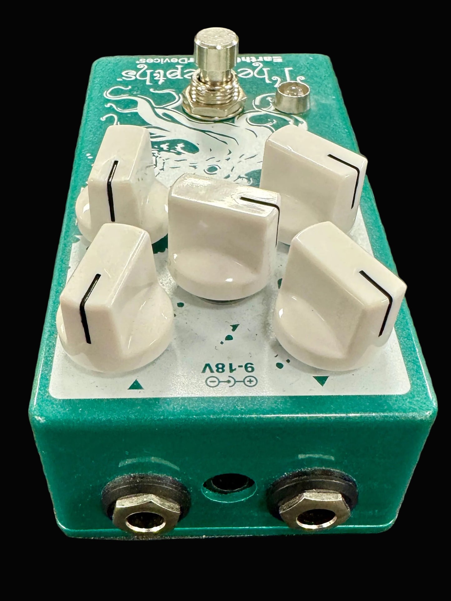 Green guitar effects pedal with white knobs on a textured surface
