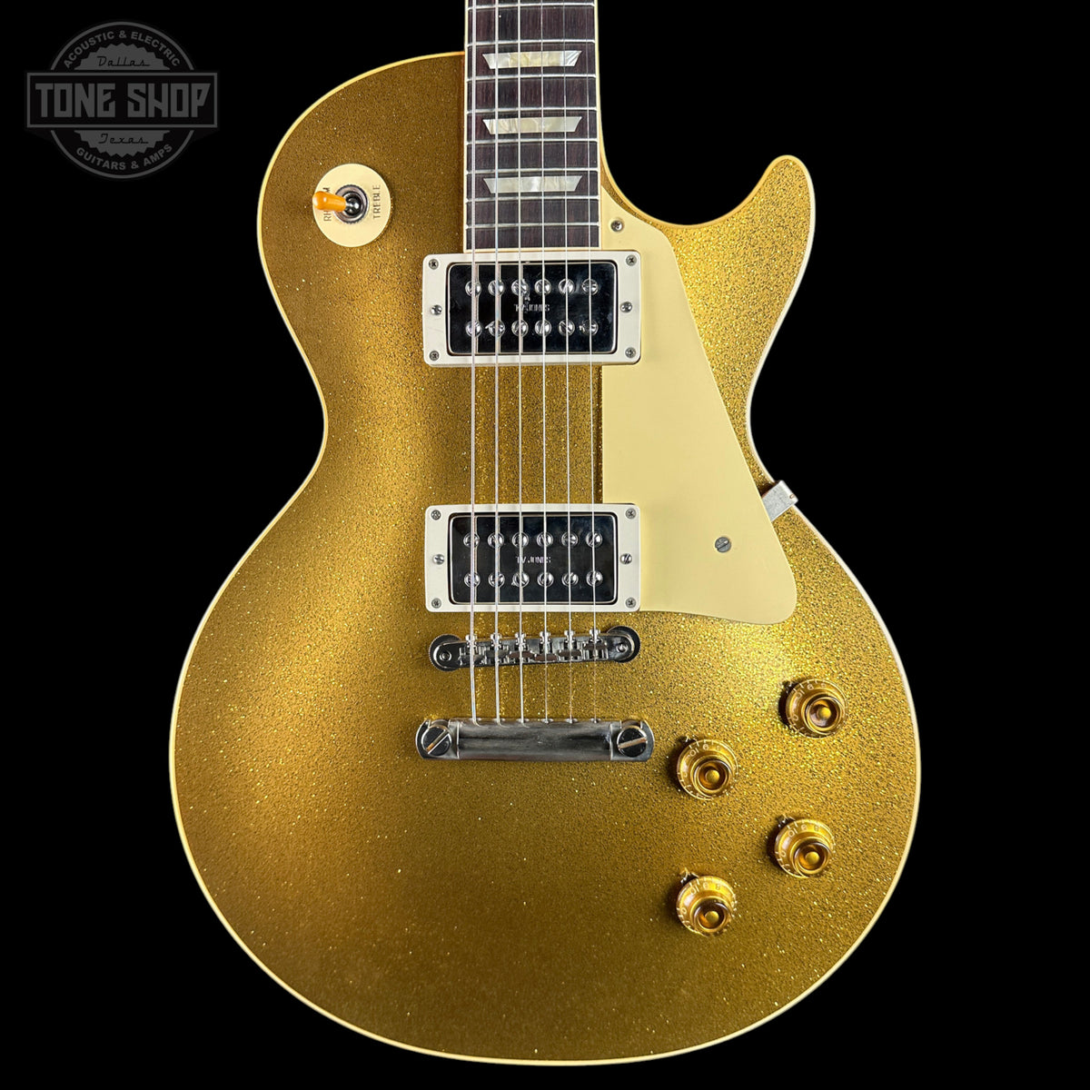 A gold-finish electric guitar with a cream pickguard and chrome hardware, shown against a solid black background. A Tone Shop watermark is visible in the top-left corner.