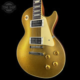A gold glitter electric guitar with a cream pickguard and chrome hardware, shown against a solid black background with a Tone Shop watermark in the top-left corner.