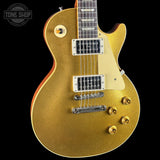 A gold glitter electric guitar with a cream pickguard and chrome hardware, shown against a solid black background with a Tone Shop watermark in the top left corner.