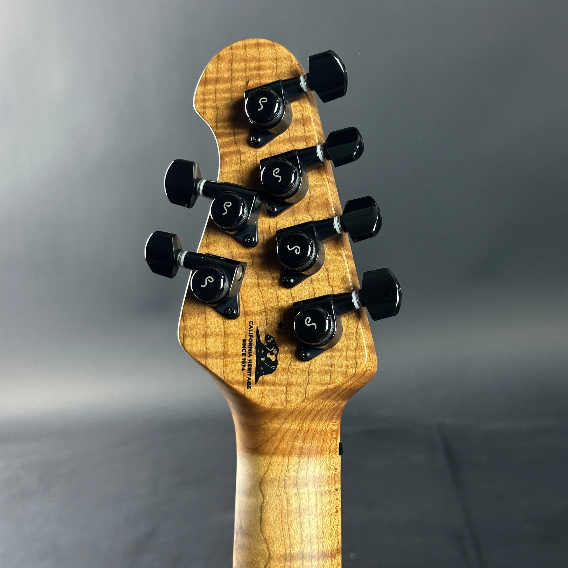 Close-up of a guitar headstock with tuning pegs on a gray background