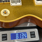Close-up of a gold glitter electric guitar body resting on a digital scale, with the scale display reading 8.134 oz and the brand WeightMax visible on the scale.