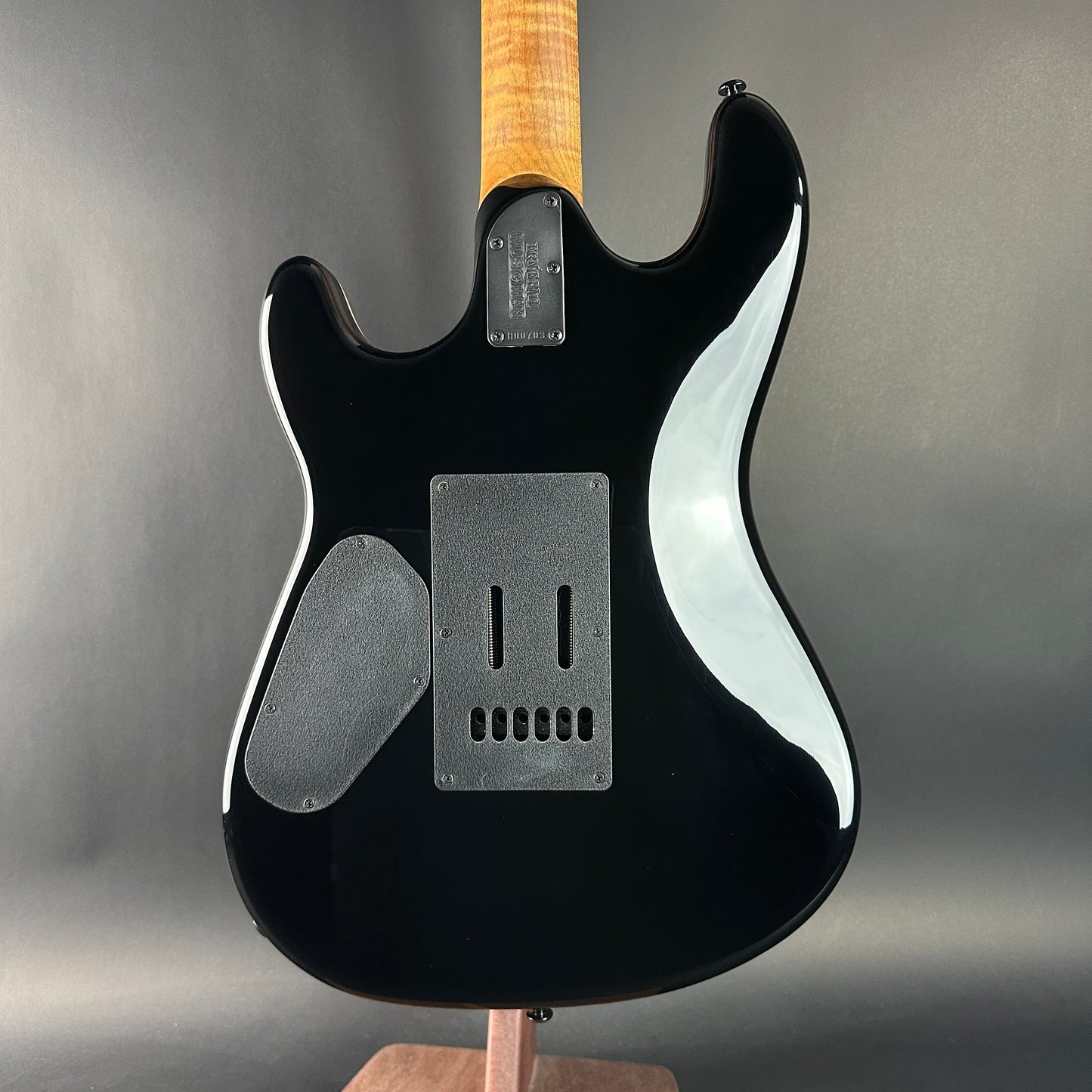 Black electric guitar with a wooden neck on a gray background