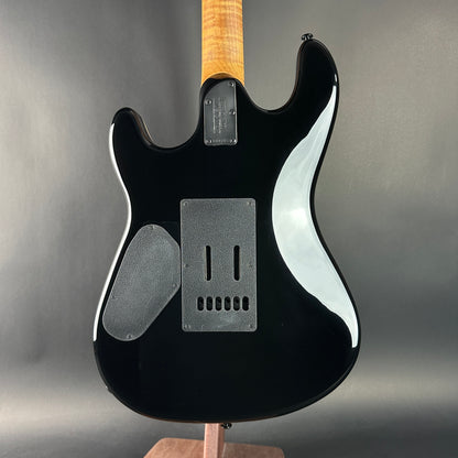 Black electric guitar with a wooden neck on a gray background