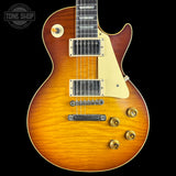 A classic electric guitar with a sunburst finish, featuring a warm orange-to-brown gradient, cream pickguard, and gold hardware, shown against a solid black background.