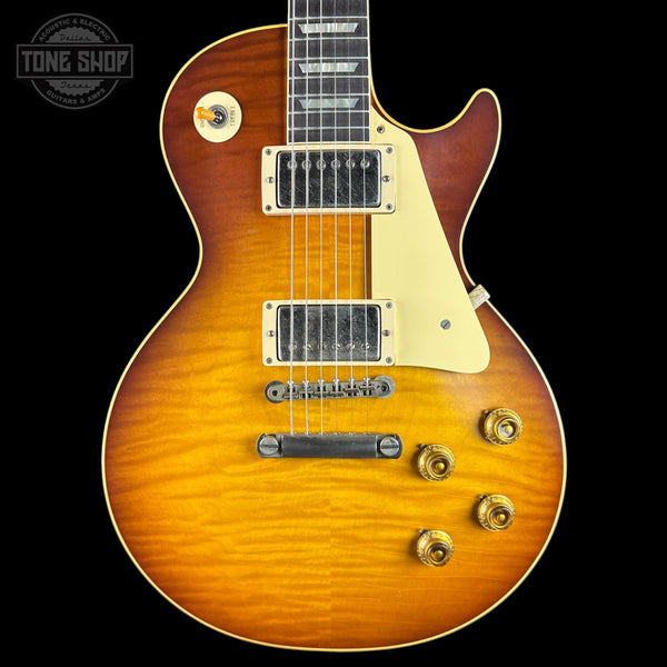 A classic electric guitar with a sunburst finish, featuring a warm orange-to-brown gradient, cream pickguard, and gold hardware, shown against a solid black background.