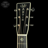 Close-up of a guitar headstock with the brand name 'CMF MARTIN' in gold lettering on a black background, with six tuning pegs and strings visible.