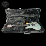 An electric guitar with a light blue and white flamed maple top, resting inside an open black hard case with a gray velvet interior. A Tone Shop watermark is visible in the top left corner.