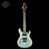 A double-cutaway electric guitar with a light blue and white flamed maple top, shown against a solid black background. The brand logo on the headstock is not clearly legible, and there is a 'TONE SHOP' watermark in the top-left corner.