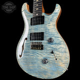 A double-cutaway electric guitar with a light blue and white flamed maple top, black hardware, and a natural wood neck, shown against a black background with a Tone Shop watermark in the top-left corner.