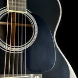 Close-up of a black acoustic guitar body with a circular soundhole, six gold-toned strings, and a glossy finish against a black background.