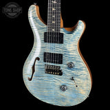 A double-cutaway electric guitar with a light blue and white flamed maple top, black pickups, and a dark fretboard, shown against a solid black background with a Tone Shop watermark in the top-left corner.