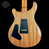 The back of an electric guitar with a natural wood grain finish, featuring black pickguards and a gold-tone bridge, shown against a solid black background with a Tone Shop watermark in the top left corner.