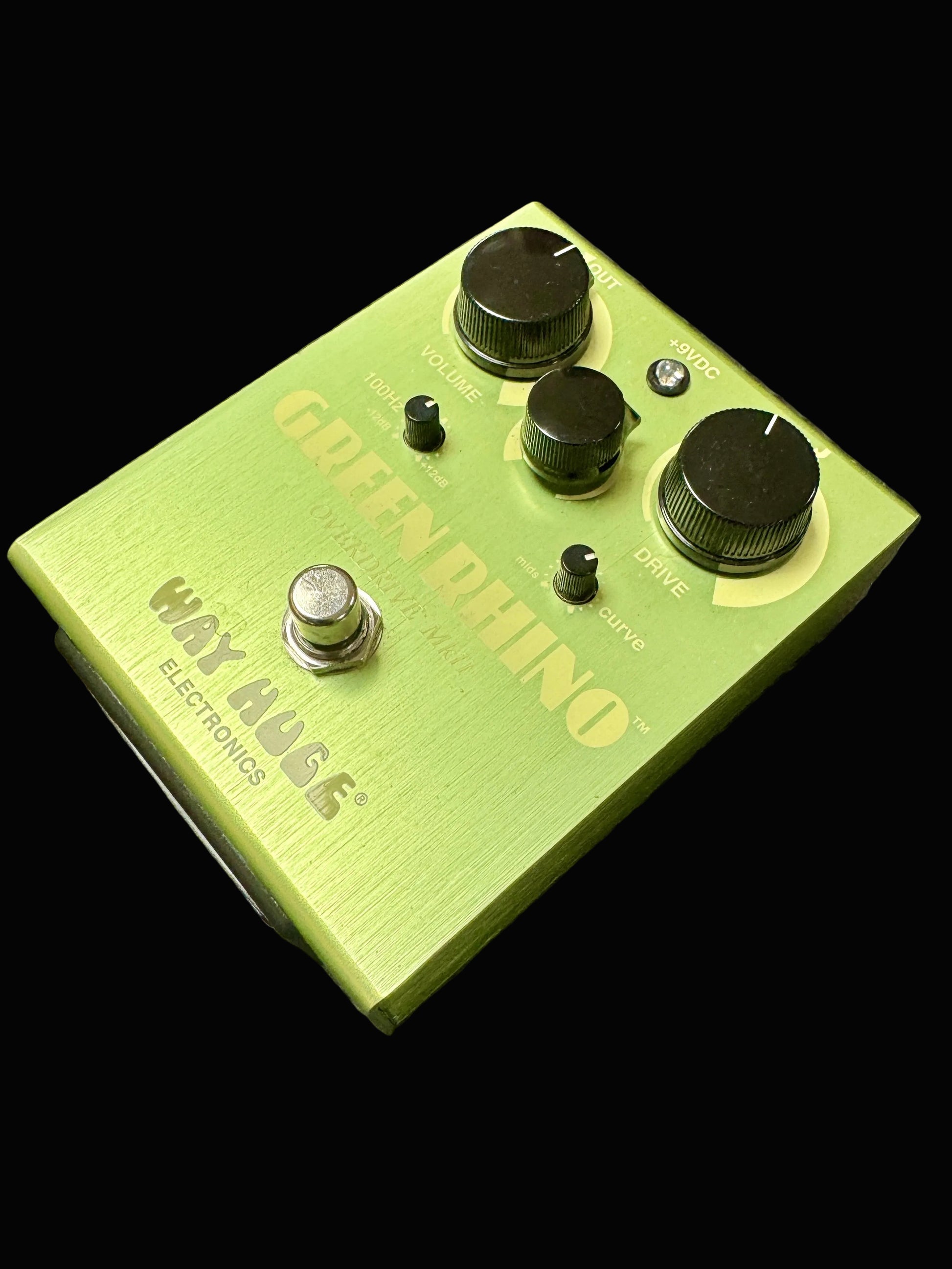 Green guitar effects pedal with knobs and labels on a textured surface