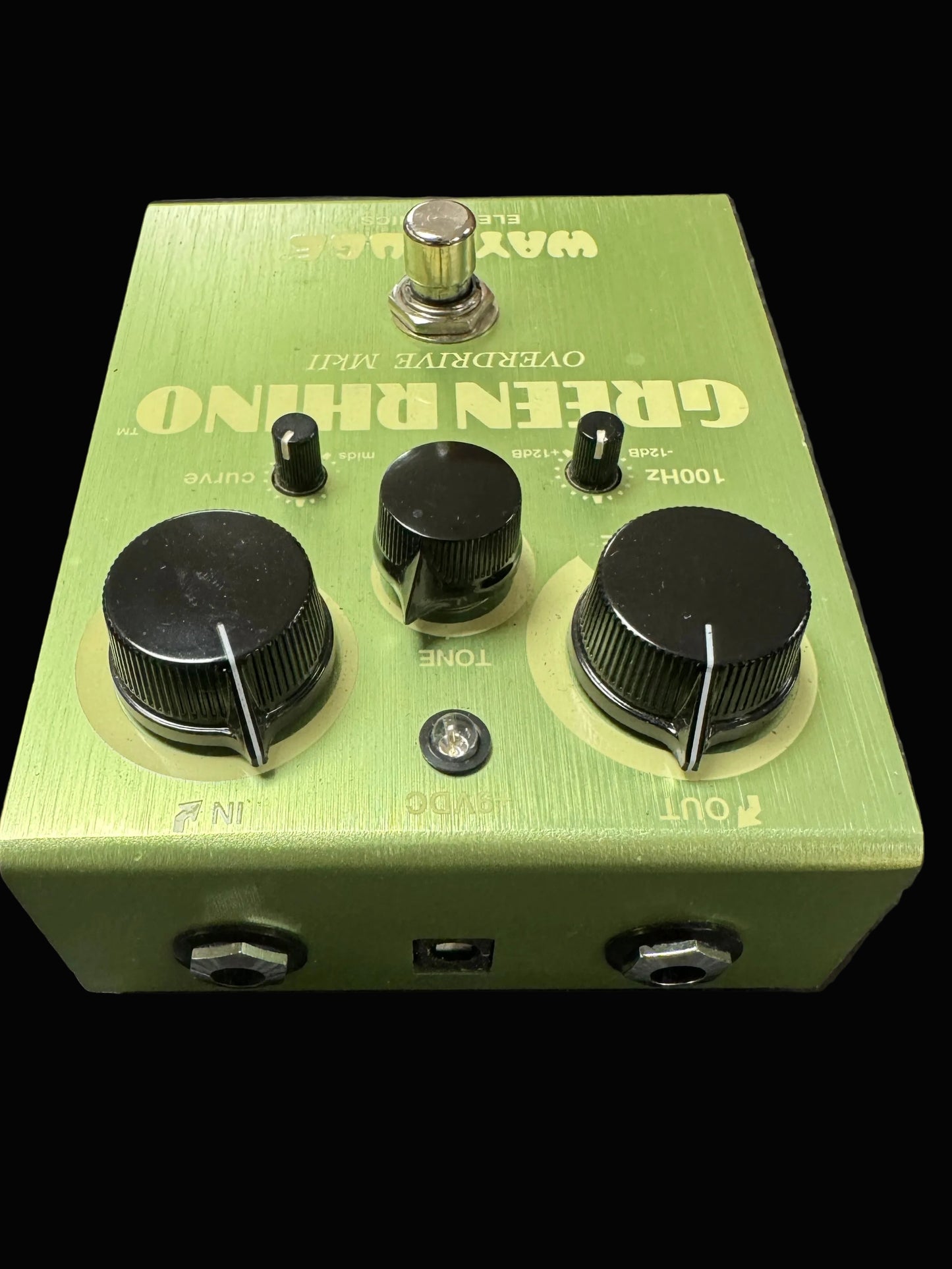 Green guitar effects pedal with knobs and labels on a textured surface