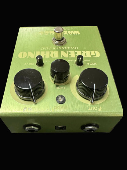 Green guitar effects pedal with knobs and labels on a textured surface