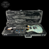 An electric guitar with a blue and green marbled quirklewood finish resting inside an open black hard case with gray velvet lining. The headstock shows the 'Squier' brand logo.