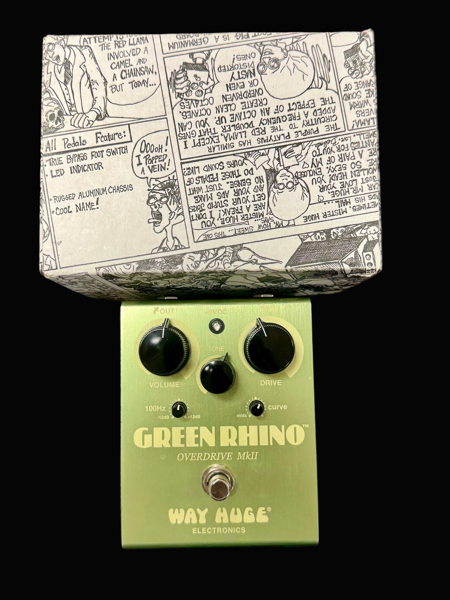 Green Rhino overdrive pedal by Way Huge Electronics on a wooden surface with comic-style packaging.