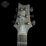 Close-up of a guitar headstock with six tuning pegs, a dark gray finish, a white script signature, and the word 'Custom' printed vertically, shown against a black background.