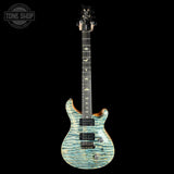 A double-cutaway electric guitar with a light blue and white tiger-flake patterned top, shown against a solid black background. A Tone Shop watermark is visible in the upper left corner.