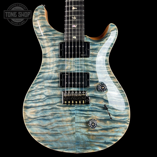A close-up of an electric guitar body with a blue and gray wavy maple wood finish, featuring black hardware and a black pickguard, shown against a solid black background with a Tone Shop watermark in the top left corner.