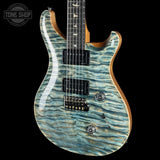 A close-up of an electric guitar body with a blue and green wavy maple wood finish, black humbucker pickups, and a black bridge, shown against a black background with a Tone Shop watermark in the top left corner.